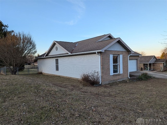 property exterior at dusk featuring brick siding, fence, and a lawn