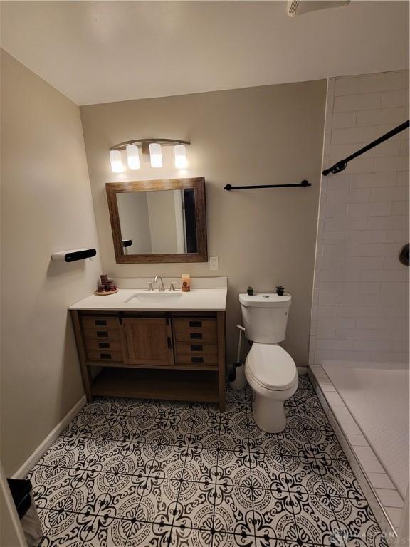 bathroom with tile patterned floors, toilet, baseboards, tiled shower, and vanity