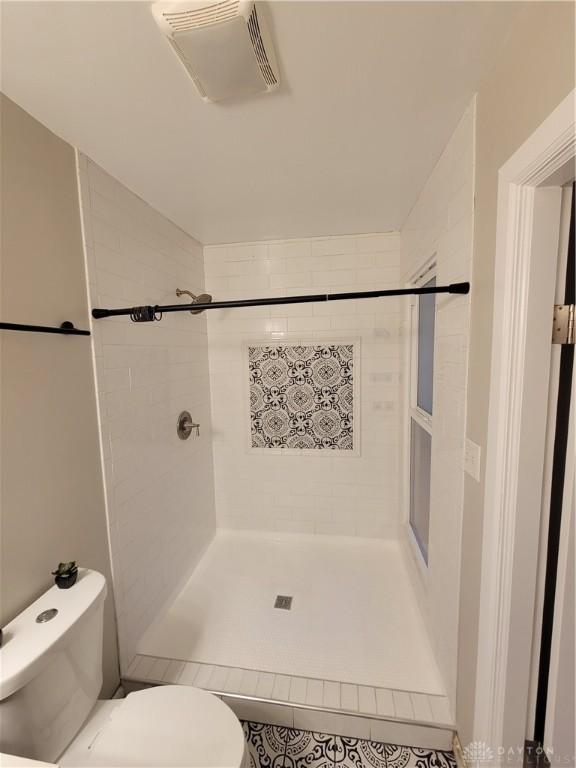 full bath with visible vents, tiled shower, and toilet