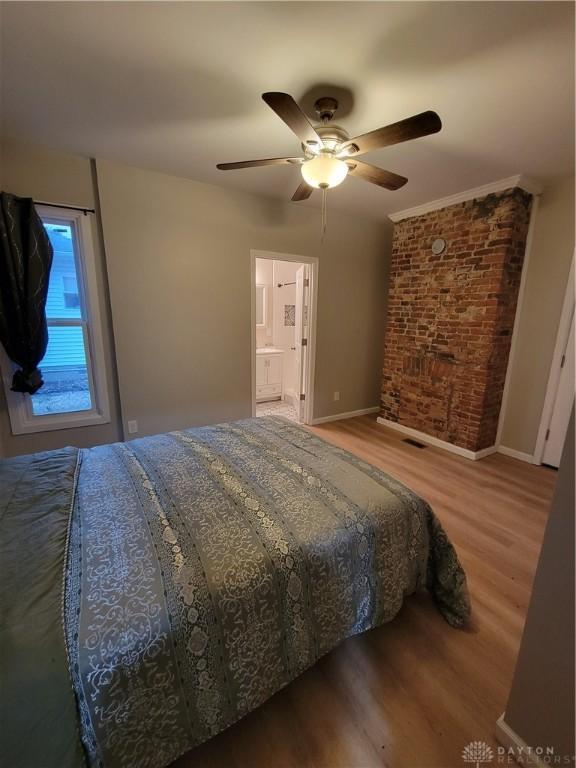 bedroom featuring ceiling fan, baseboards, wood finished floors, and brick wall