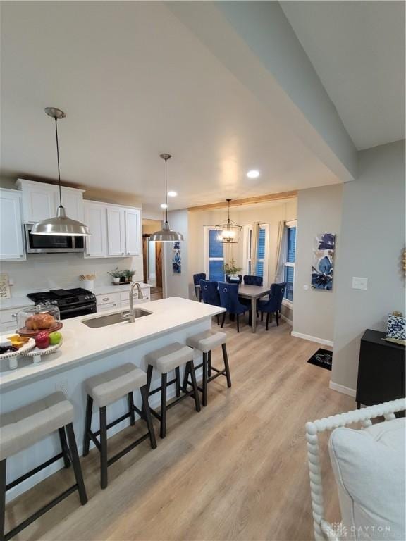 kitchen with black gas range oven, stainless steel microwave, a kitchen bar, white cabinets, and a sink