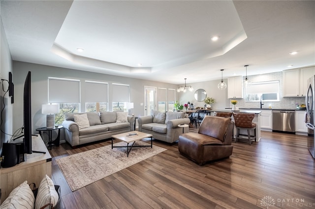 living area featuring a raised ceiling, recessed lighting, dark wood-style floors, and a chandelier