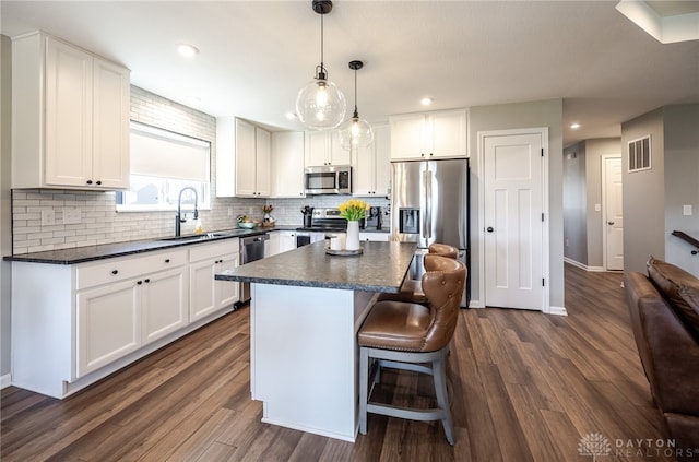 kitchen featuring visible vents, a kitchen island, a sink, stainless steel appliances, and dark countertops