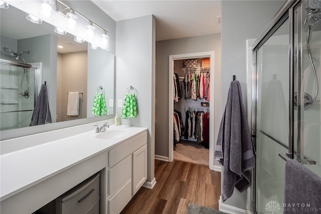 full bathroom featuring a spacious closet, baseboards, a stall shower, wood finished floors, and vanity