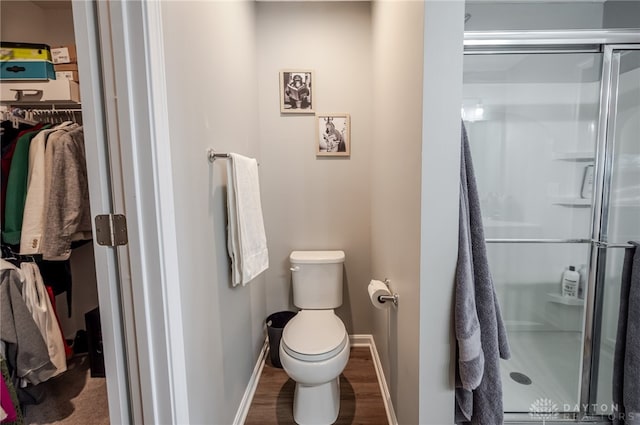 bathroom with a shower stall, toilet, baseboards, and wood finished floors