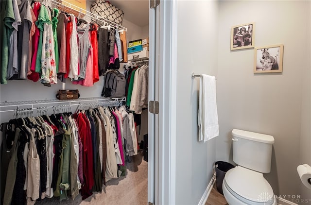 bathroom featuring a walk in closet, toilet, and baseboards