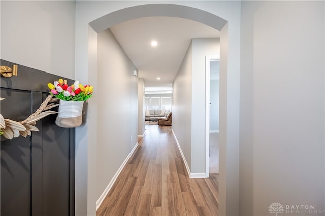 hallway featuring arched walkways, recessed lighting, baseboards, and wood finished floors