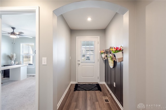 doorway featuring arched walkways, visible vents, a ceiling fan, and baseboards