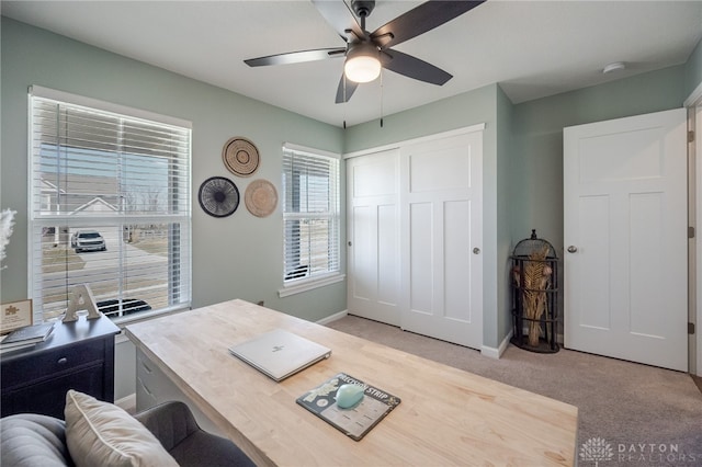 home office featuring light colored carpet, baseboards, and ceiling fan