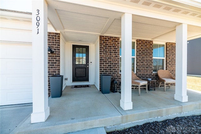 view of exterior entry with brick siding and a porch