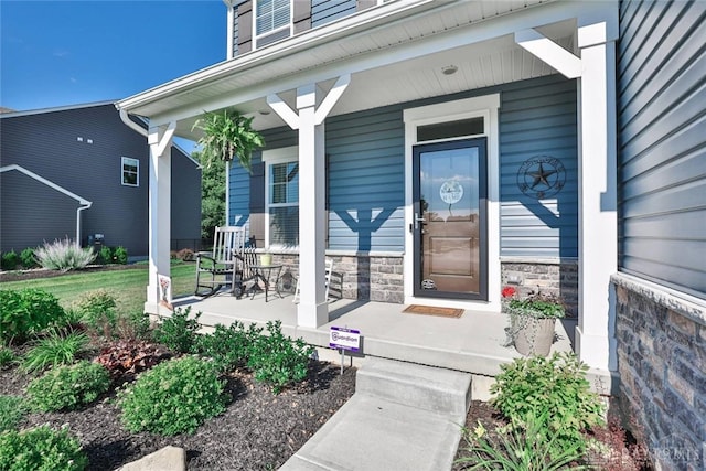 view of exterior entry featuring stone siding and covered porch