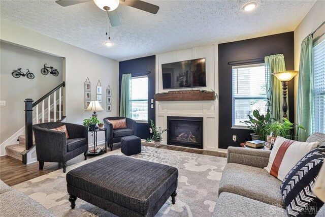 living room with wood finished floors, ceiling fan, stairs, a textured ceiling, and a glass covered fireplace