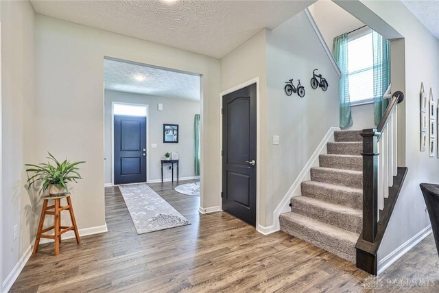 entryway with a textured ceiling, stairs, baseboards, and wood finished floors