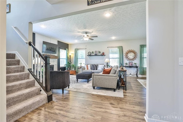 living area featuring stairway, a ceiling fan, wood finished floors, a fireplace, and a textured ceiling