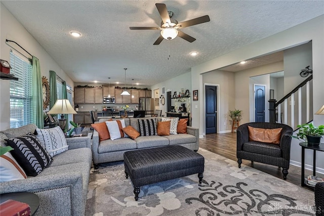 living area featuring a textured ceiling, stairway, light wood finished floors, baseboards, and ceiling fan