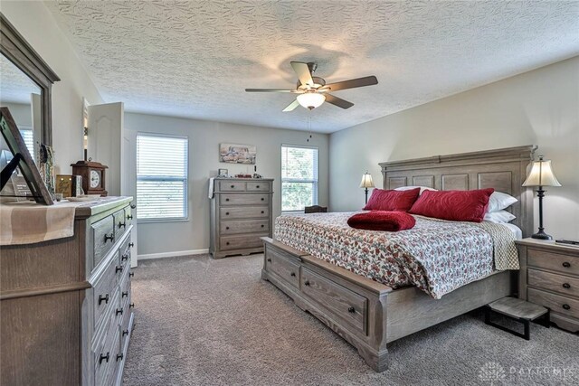 bedroom with a textured ceiling, light colored carpet, baseboards, and ceiling fan