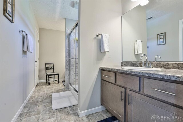 bathroom featuring vanity, baseboards, visible vents, a shower stall, and a textured ceiling