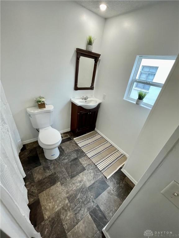 bathroom with vanity, baseboards, stone finish flooring, a textured ceiling, and toilet