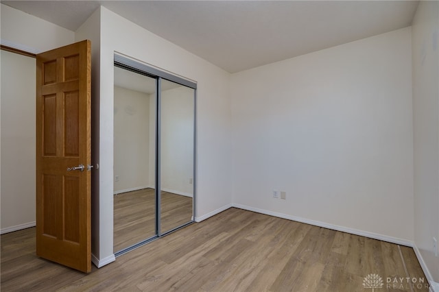 unfurnished bedroom featuring wood finished floors, a closet, and baseboards