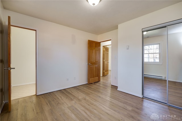 unfurnished bedroom featuring a baseboard radiator, baseboards, a closet, and light wood finished floors