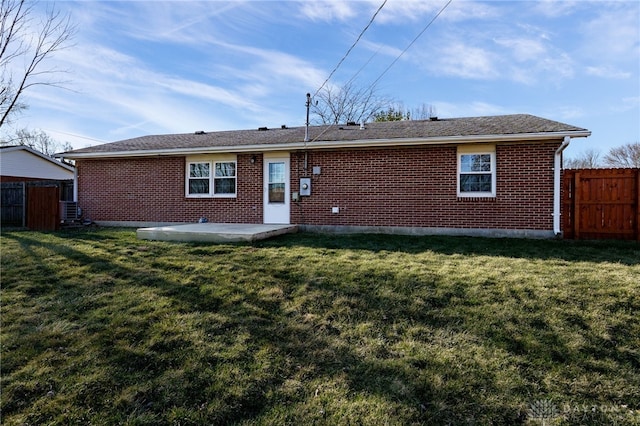 rear view of property featuring brick siding, a patio area, a yard, and fence