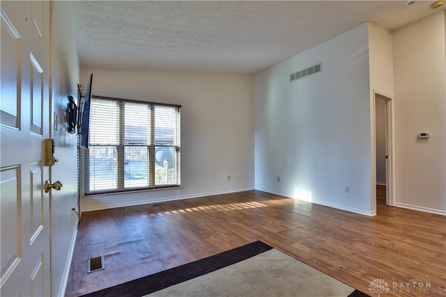 empty room featuring visible vents, a textured ceiling, and wood finished floors