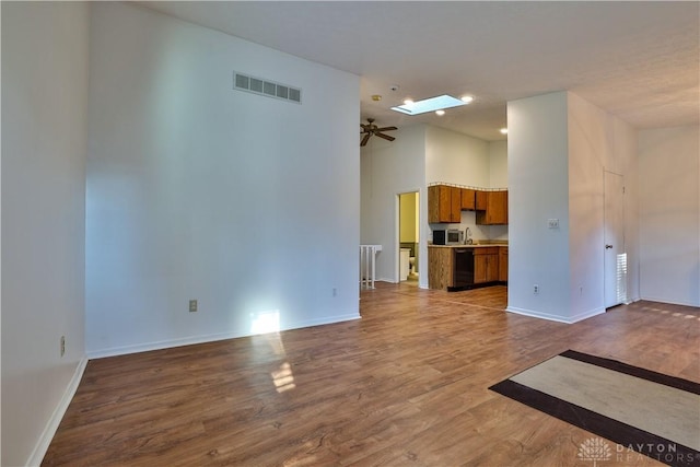 unfurnished living room with visible vents, a skylight, baseboards, ceiling fan, and dark wood-style flooring