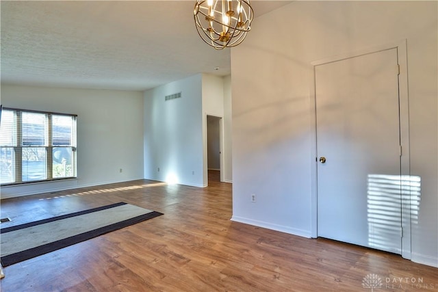 unfurnished room with visible vents, a textured ceiling, wood finished floors, an inviting chandelier, and baseboards