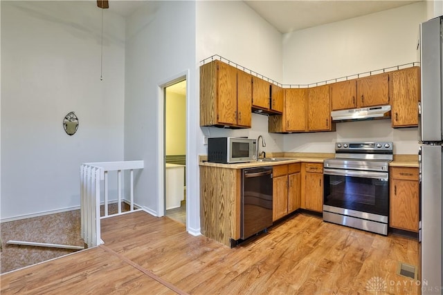 kitchen featuring a sink, brown cabinets, under cabinet range hood, and stainless steel appliances