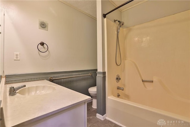 bathroom featuring toilet, a textured ceiling, shower / washtub combination, wainscoting, and vanity