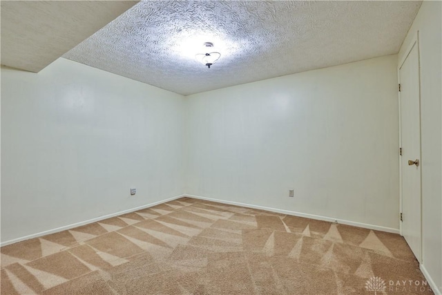 empty room with a textured ceiling, baseboards, and light carpet