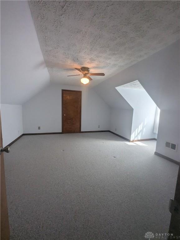 bonus room featuring vaulted ceiling, carpet flooring, baseboards, and a textured ceiling