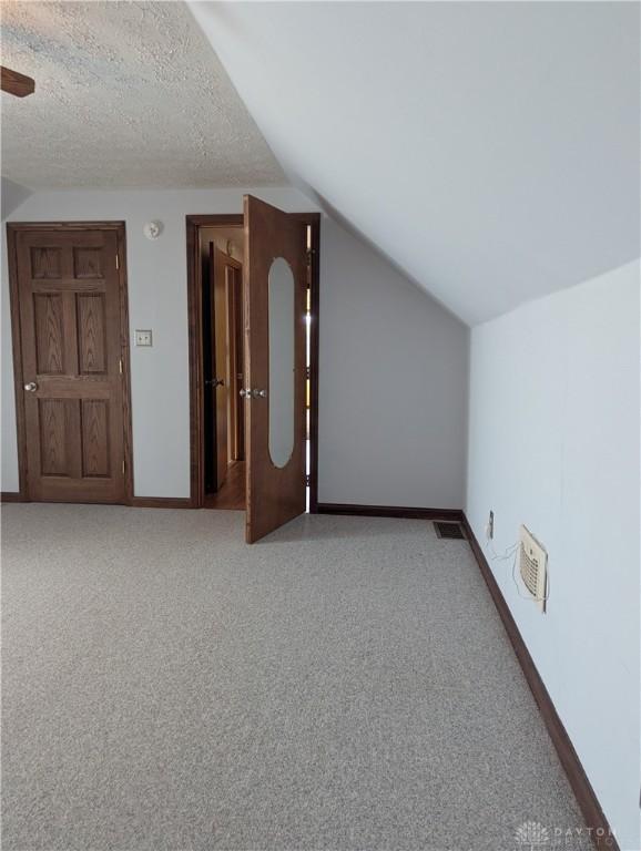 bonus room featuring carpet, baseboards, visible vents, vaulted ceiling, and a textured ceiling