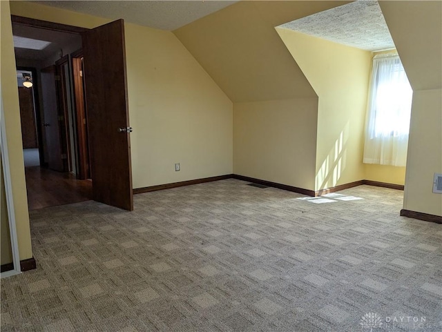 additional living space with carpet flooring, a textured ceiling, baseboards, and vaulted ceiling