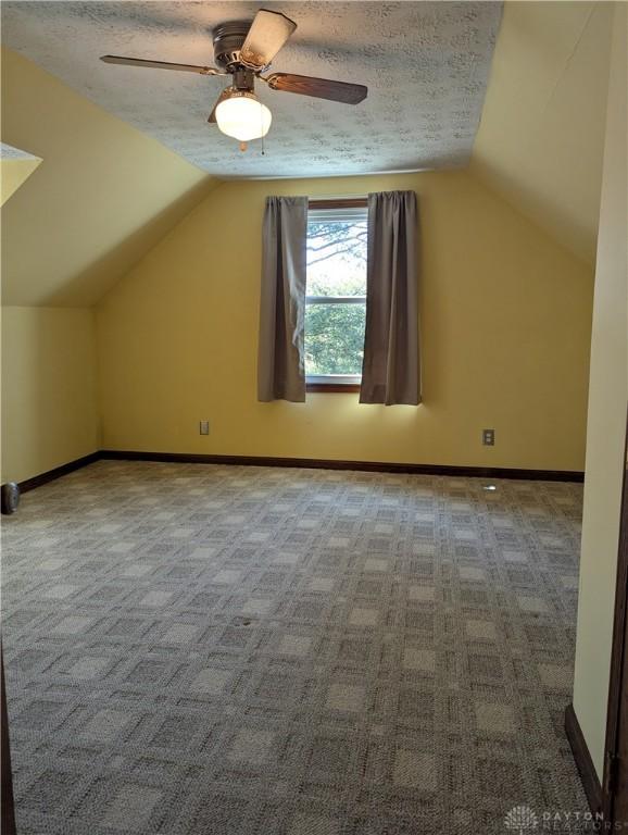 bonus room with baseboards, a textured ceiling, vaulted ceiling, and carpet