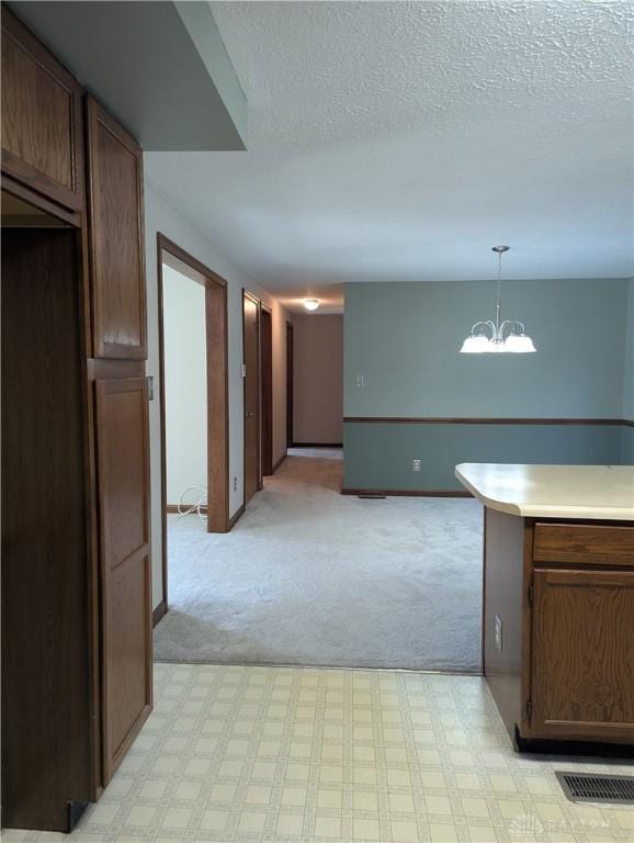 kitchen featuring visible vents, light countertops, pendant lighting, a textured ceiling, and a notable chandelier