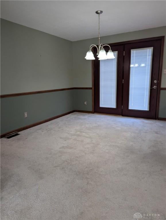 carpeted empty room featuring visible vents, baseboards, and a notable chandelier