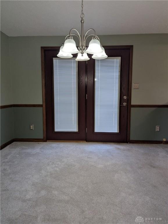 empty room with an inviting chandelier, light colored carpet, and baseboards