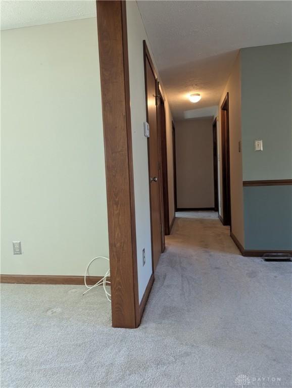 hall featuring light colored carpet, baseboards, and a textured ceiling