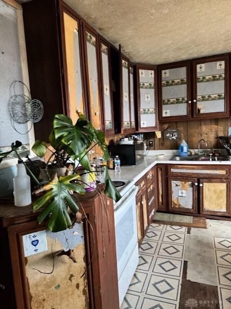 kitchen featuring a sink, electric range, glass insert cabinets, and light countertops