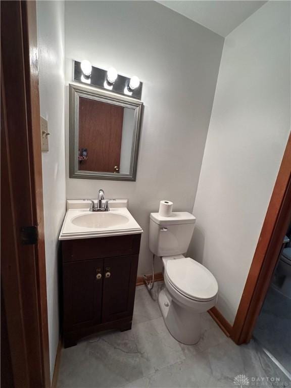 half bathroom featuring vanity, toilet, and baseboards