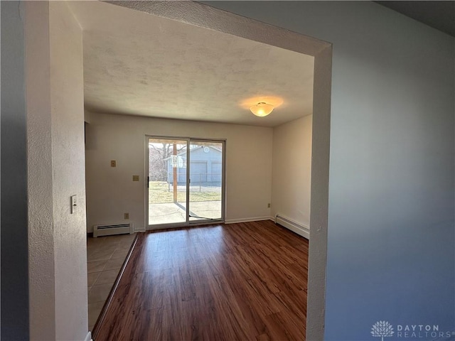 empty room featuring a textured ceiling, a baseboard heating unit, baseboards, and wood finished floors