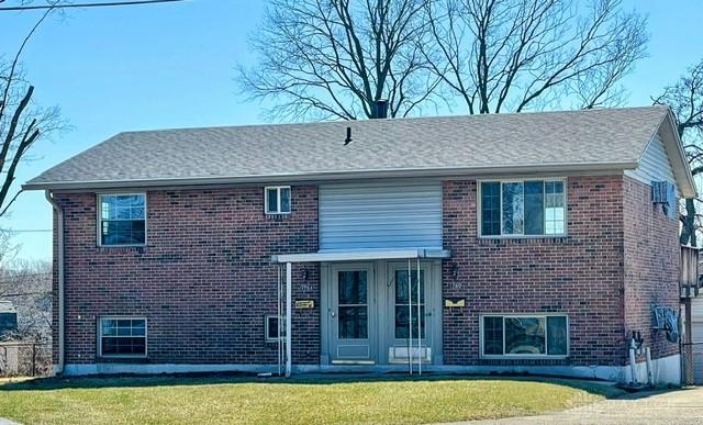 back of property with concrete driveway, a lawn, and brick siding