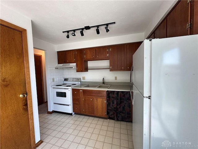 kitchen with a sink, under cabinet range hood, white appliances, light countertops, and decorative backsplash