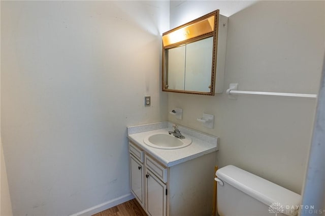 half bath featuring vanity, toilet, wood finished floors, and baseboards