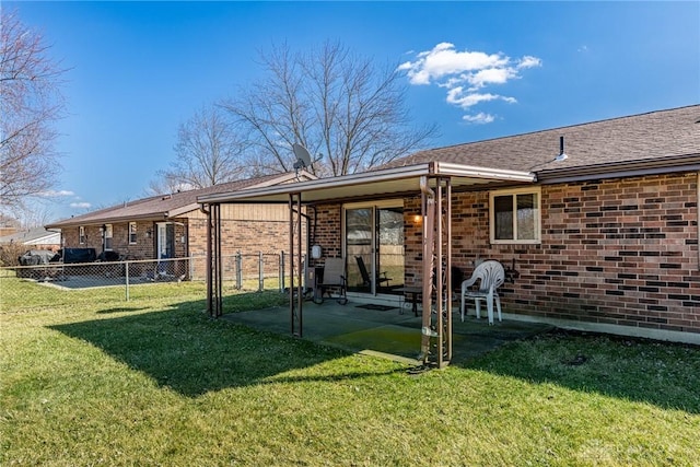 back of house featuring fence, a yard, roof with shingles, brick siding, and a patio area