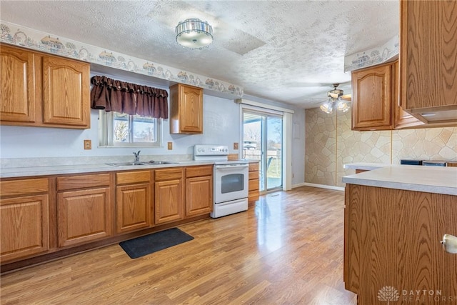 kitchen featuring a sink, light countertops, light wood-type flooring, and white range with electric stovetop