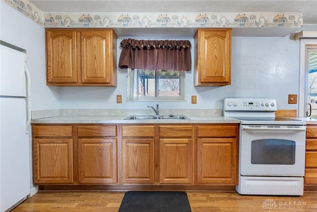 kitchen with a sink, light wood-type flooring, white appliances, and light countertops