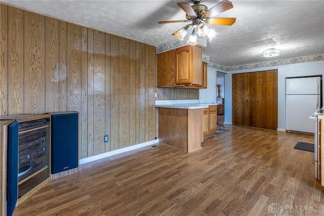 kitchen with light countertops, brown cabinets, freestanding refrigerator, wood finished floors, and a textured ceiling