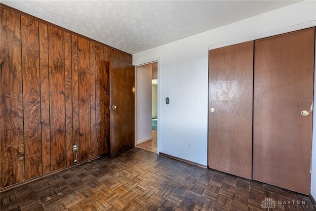 unfurnished bedroom featuring a closet, baseboards, a textured ceiling, and wood walls